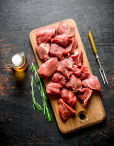 Sliced raw beef with rosemary, fork and bottled oil. On rustic background